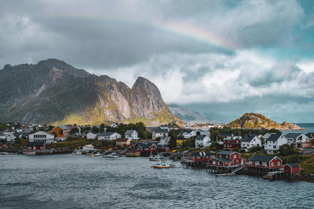 A stunning view of Reine village in Lofoten, Norway, with red cabins, a rainbow, and majestic mountains.