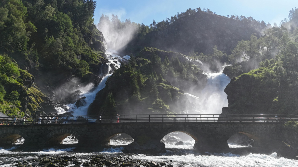 A stunning waterfall cascading down a rocky landscape, captured on a sunny day in Norway.