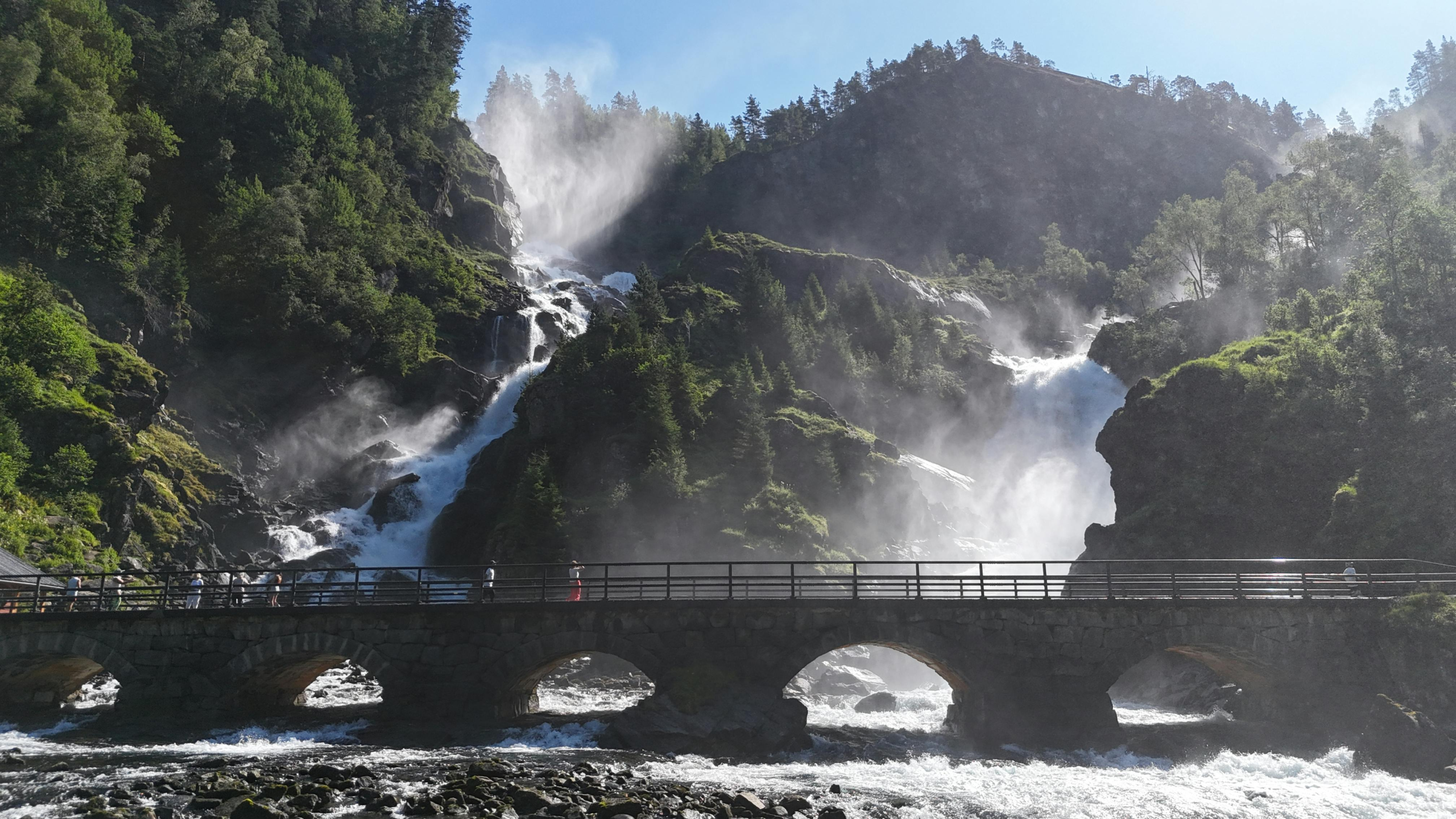 A stunning waterfall cascading down a rocky landscape, captured on a sunny day in Norway.